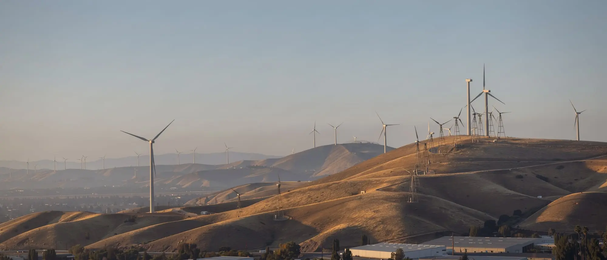 Wind turbines on the golden hills of the Altamont Pass at sunrise, with the valley floor below